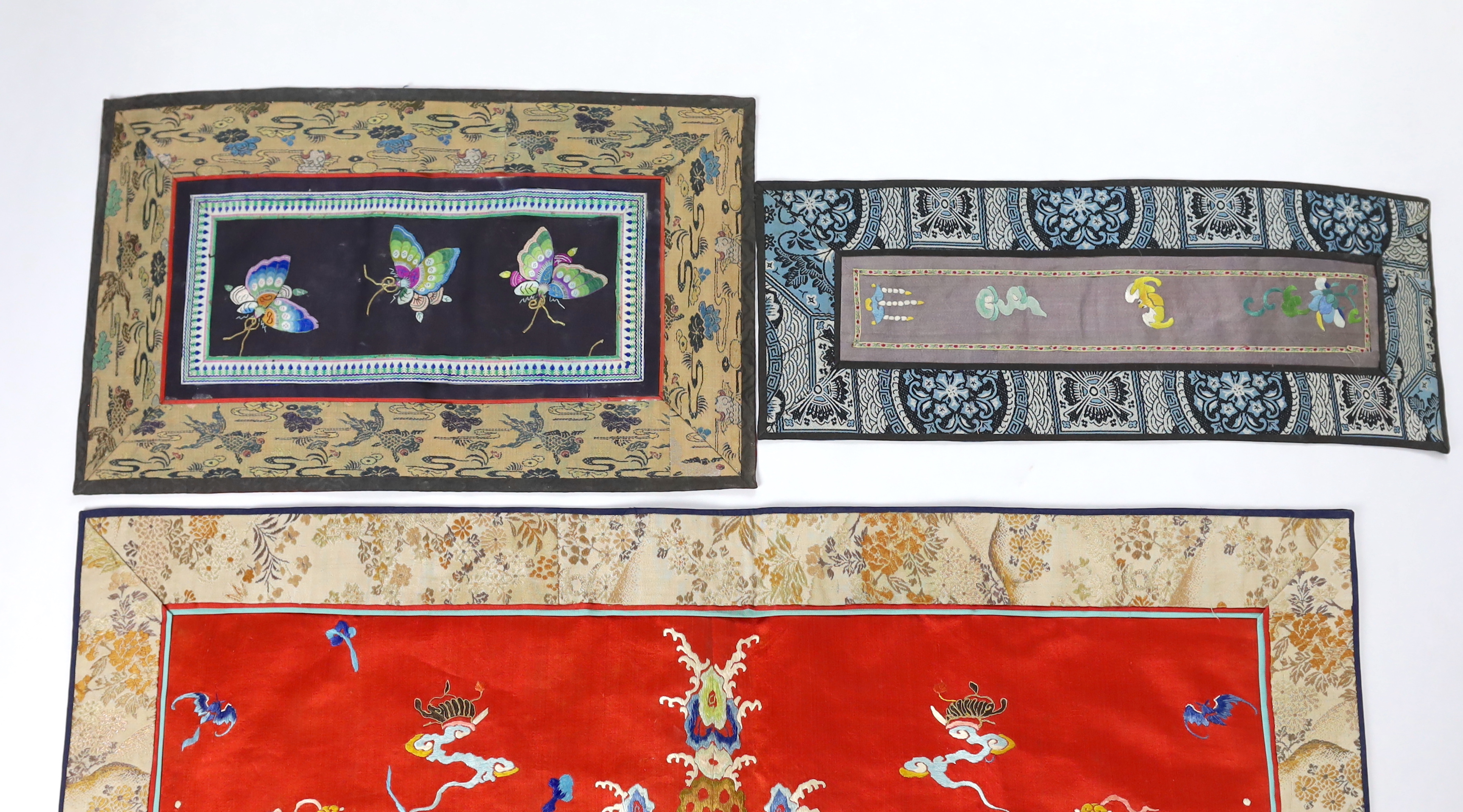 A Chinese late Qing dynasty red silk and polychrome embroidered lishui wave and flaming pearl panel, another smaller metallic dragon panel, an ornate butterfly panel and two other smaller embroidered panels with auspicio